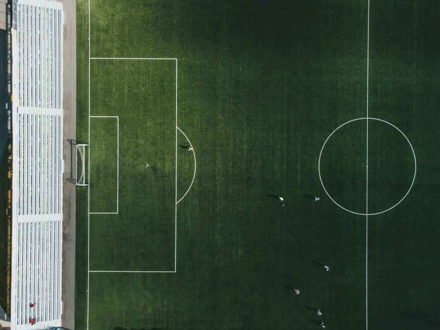 Vista aérea de um campo de futebol com jogadores em ação durante uma partida.