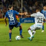 Jogadores disputam a bola durante uma partida de futebol em um gramado.