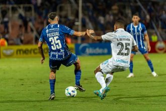 Jogadores disputam a bola durante uma partida de futebol em um gramado.