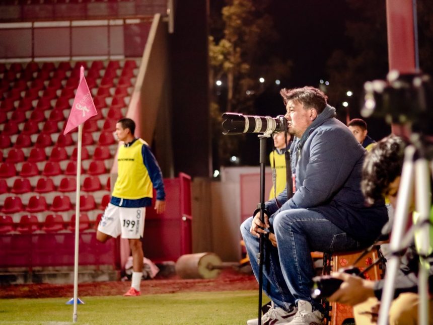 Treinador de futebol observa atentamente uma partida à noite, à beira do campo.