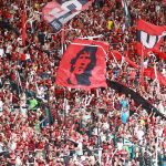 Torcedores do Flamengo, vestidos de vermelho e preto, comemoram nas arquibancadas do Maracanã.